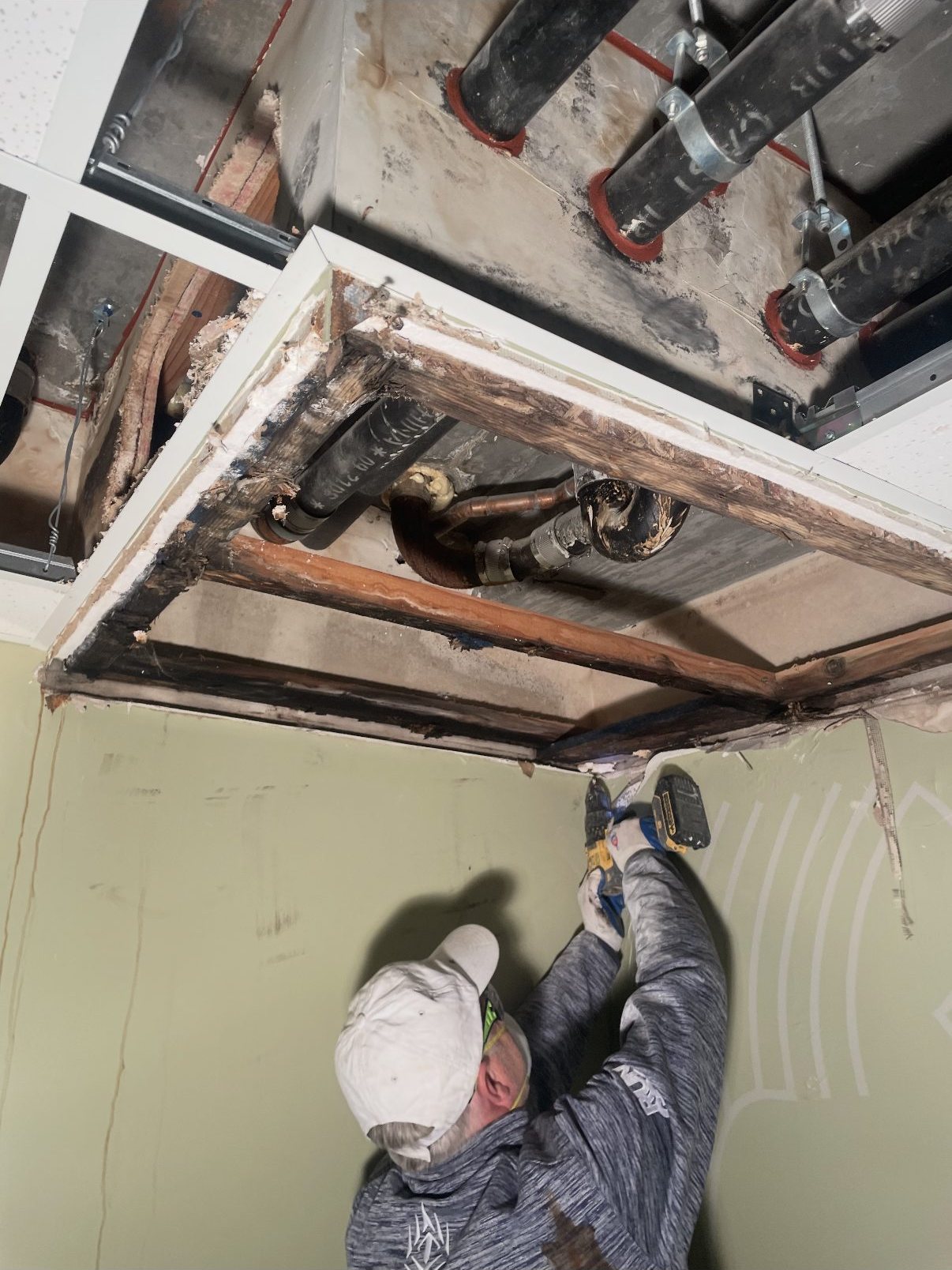 Worker removing compromised ceiling material around the leak